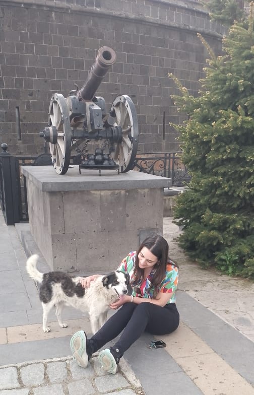 Christine sitting on the cobblestones at the Black Fortress in Gyumri, gently meeting Gilbert the stray dog for the first time